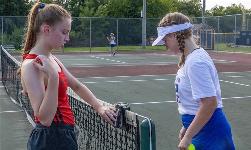 Two tennis players stand near the net
